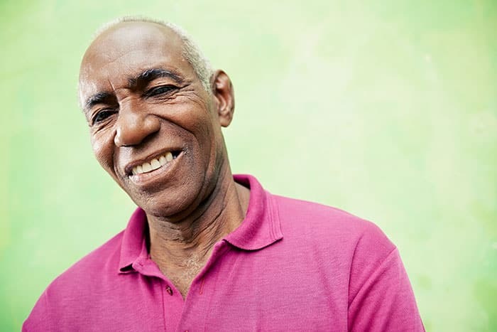 Smiling man in pink polo shirt against green background for dental practice patient testimonial.