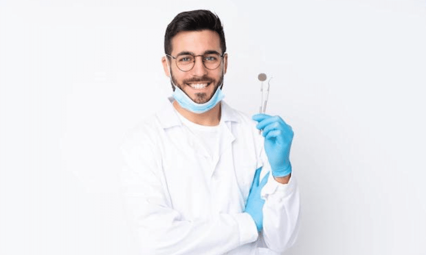 Young male dentist holding dental mirror tool wearing white coat and blue gloves.