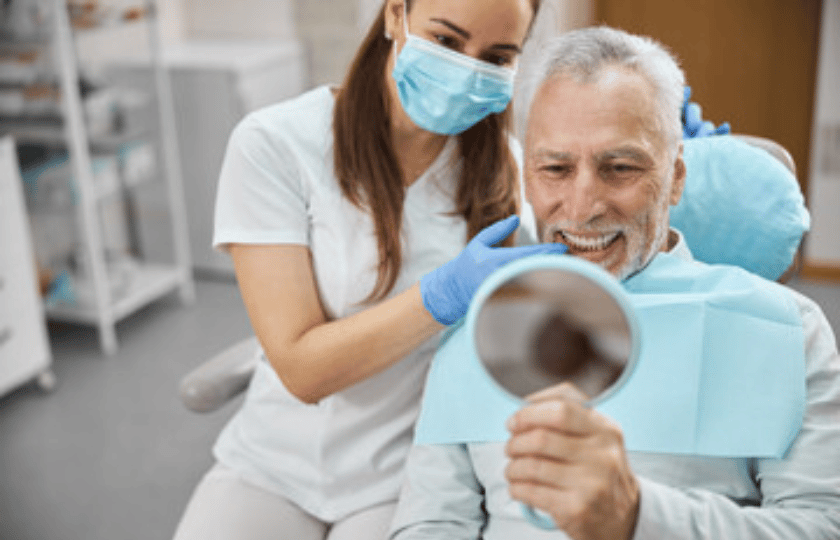 Is A Dental Implant Right For You Senior man viewing his smile in mirror with female dentist in Phoenix dental office.
