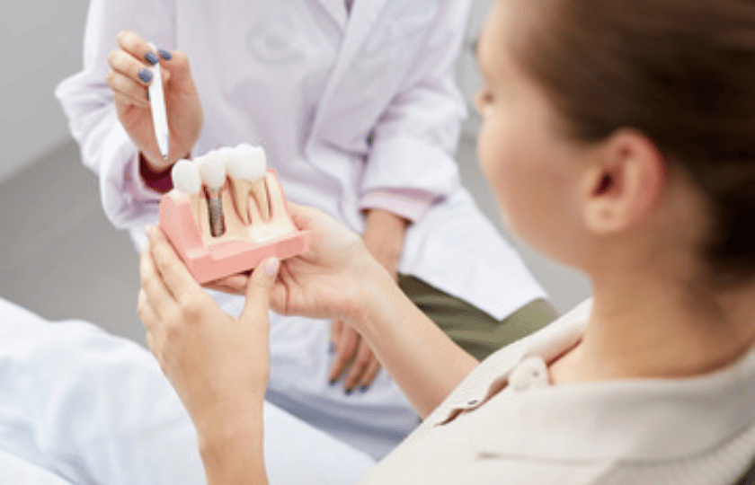 Managing Pain And Discomfort After Dental Implant Dentist showing dental implant model to patient during post-procedure consultation.