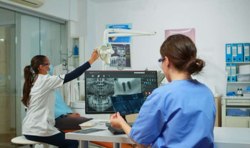 Dental professional reviewing panoramic X-ray with colleague during CT scan consultation for root canal treatment planning.
