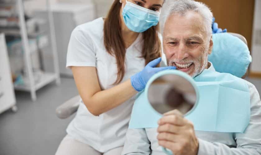 Boost Your Confidence: Celebrate Independence Day with Dental Implants Senior patient admiring his smile in mirror with dentist at Phoenix dental practice.