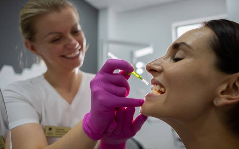 Periodontist in Phoenix (2) (1) Dentist in purple gloves applying bone graft material to patient's teeth during periodontal procedure.