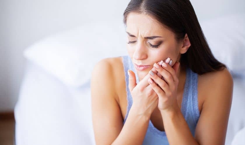 Woman holding her cheek in pain, illustrating symptoms of periodontal disease.