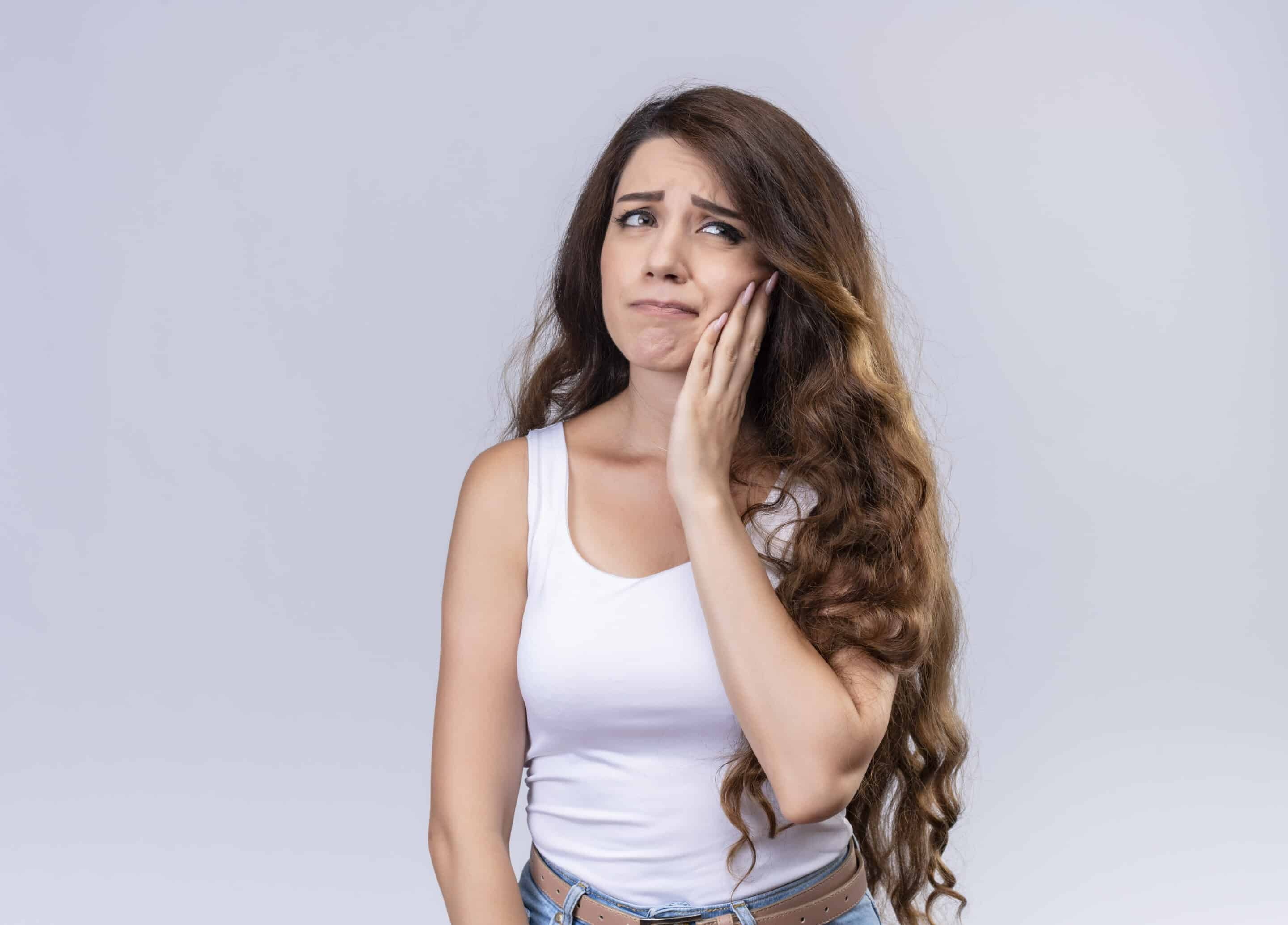 aching young beautiful girl putting hand on cheek suffering from toothache on isolated white background with copy space Woman with hand to cheek showing discomfort, illustrating gum disease symptoms.