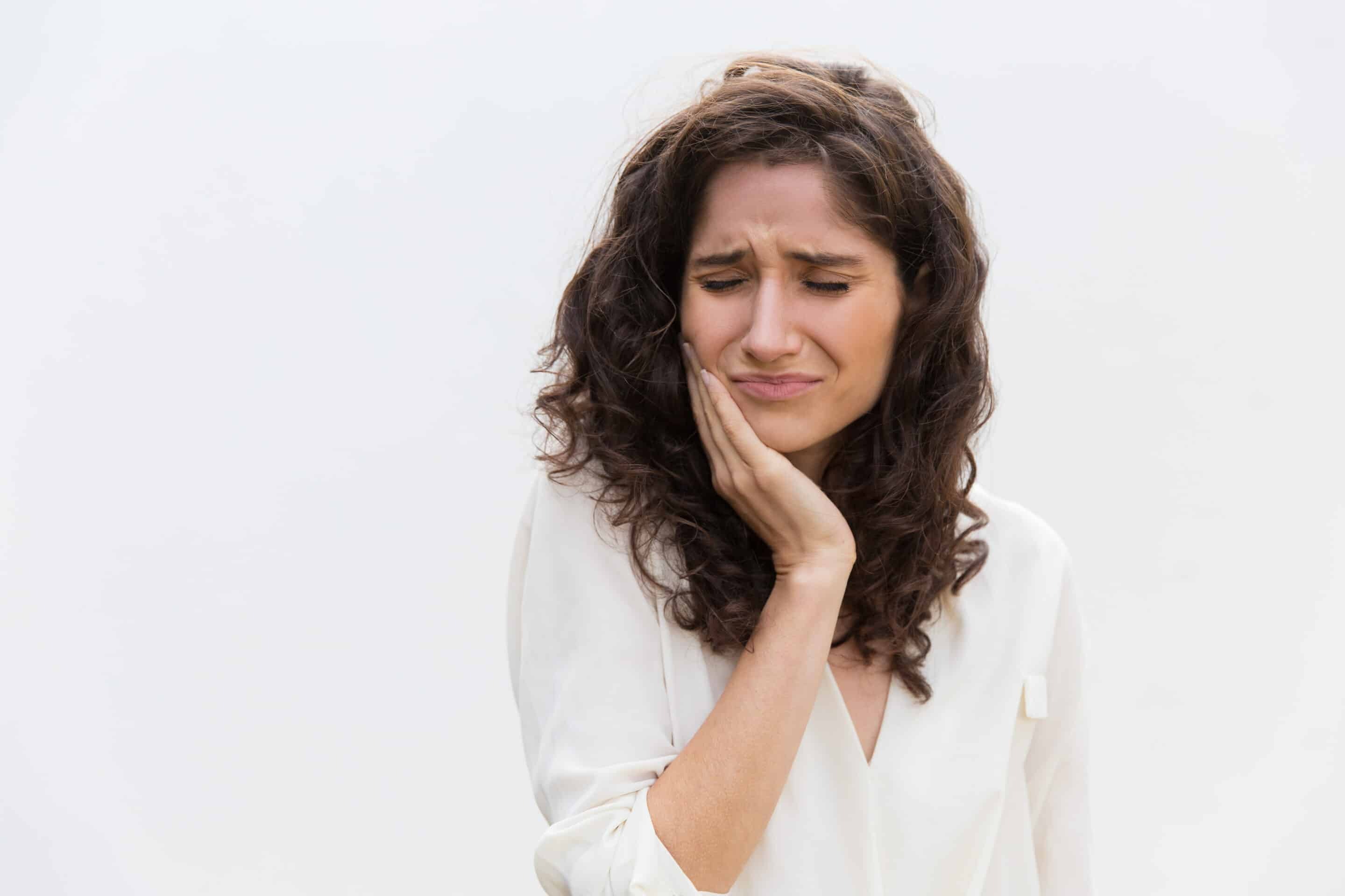Woman with tooth pain holding her cheek, illustrating gum disease symptoms requiring dental screening.