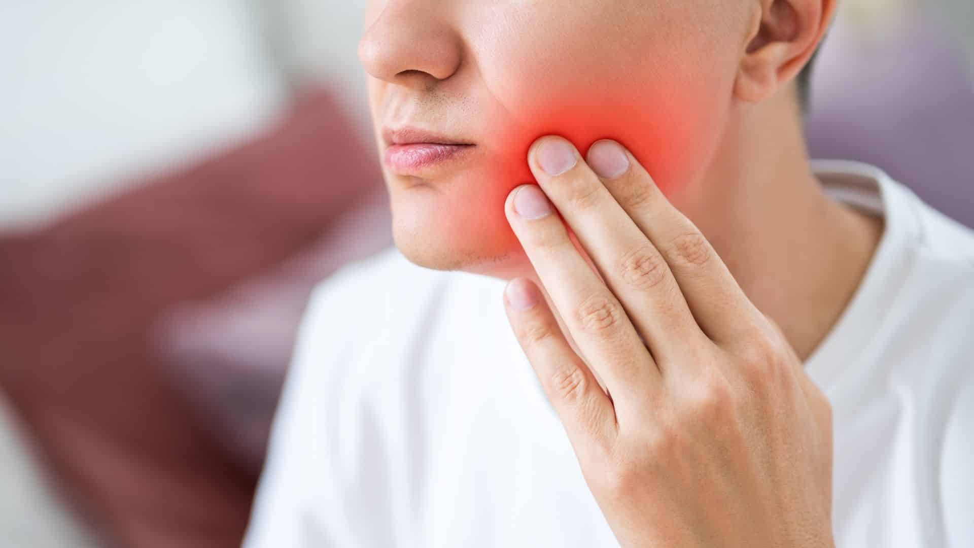 Types of Gum Disease Man experiencing jaw pain and gum disease symptoms, holding cheek with red inflammation highlighted.