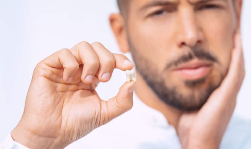 Man holding broken tooth, experiencing dental pain after extraction.