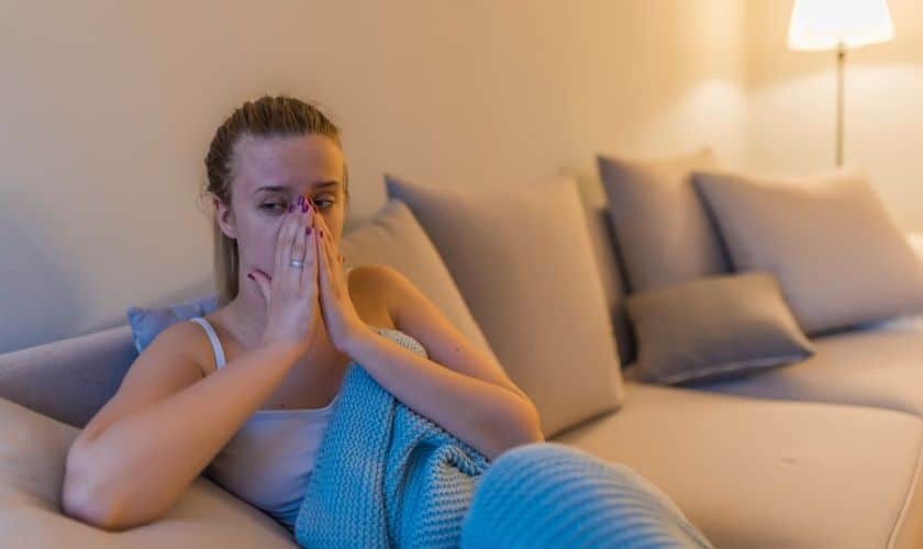 Sinus Graft Surgery Woman holding her face in discomfort on a couch, illustrating post-surgical pain after sinus graft procedure.