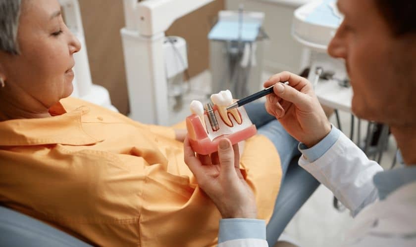 Dentist showing patient a dental implant model during tooth replacement consultation.