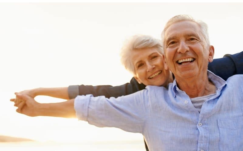 Happy senior couple smiling outdoors, representing long-term health with dental implants.