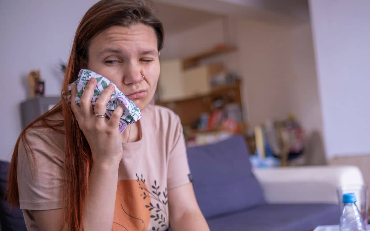 Your Gums And Prevent Gum Disease Woman holding tissue to her face while looking at laptop, concerned about gum health.