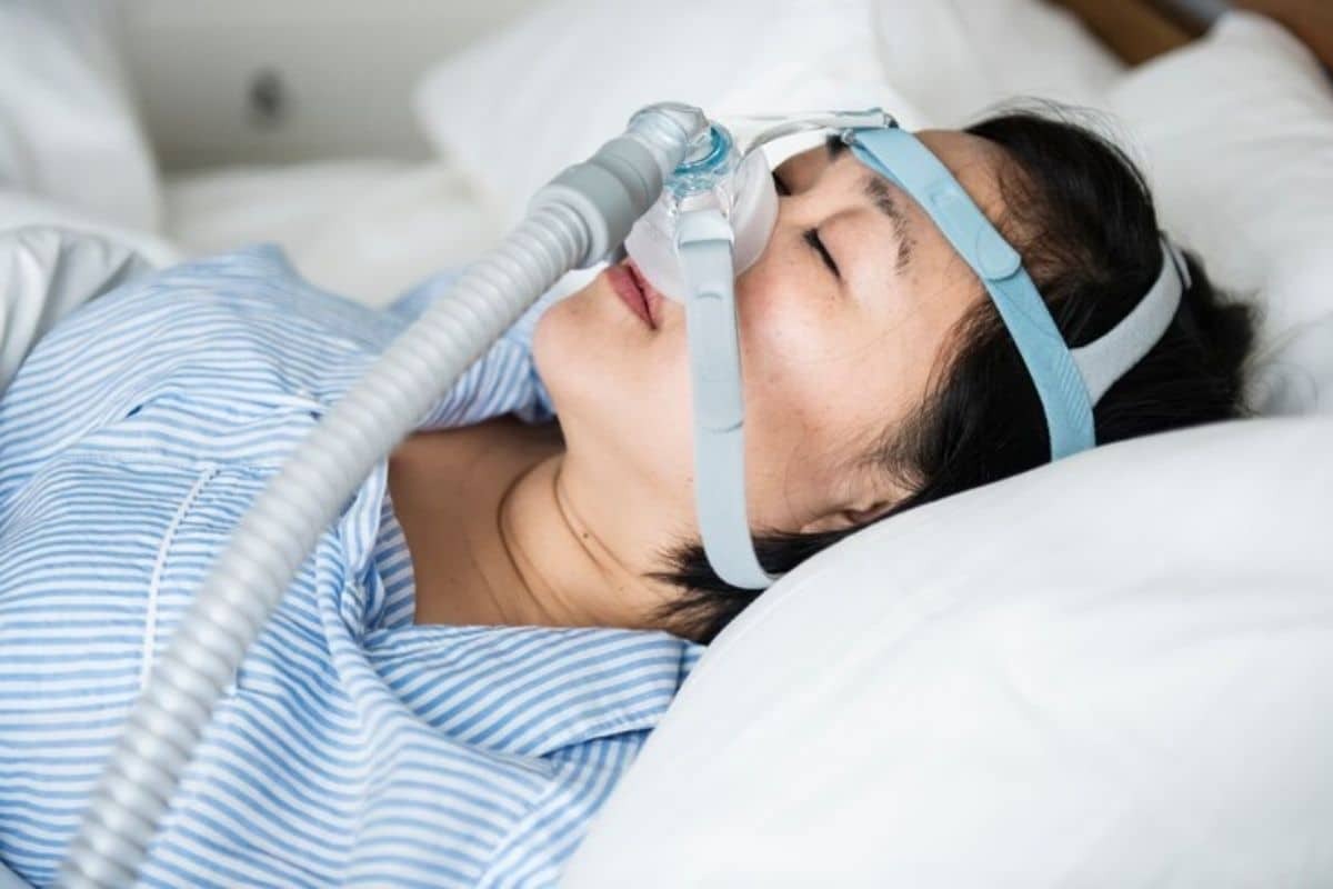 Man wearing CPAP mask sleeping peacefully in bed for dental sedation context.