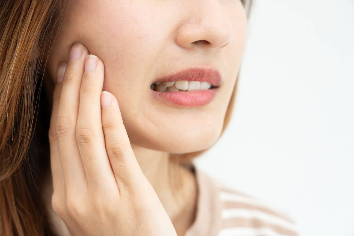 Top 5 Patient Questions on Gum Recession Treatments Woman touching her cheek, showing signs of gum recession or tooth sensitivity.