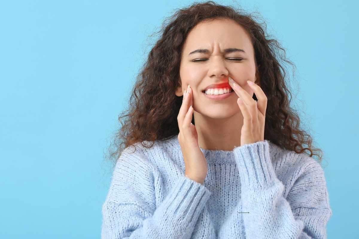 Gum Lump Causes & Warning Signs Woman with gum pain touching her mouth, illustrating dental concerns like gum lumps.
