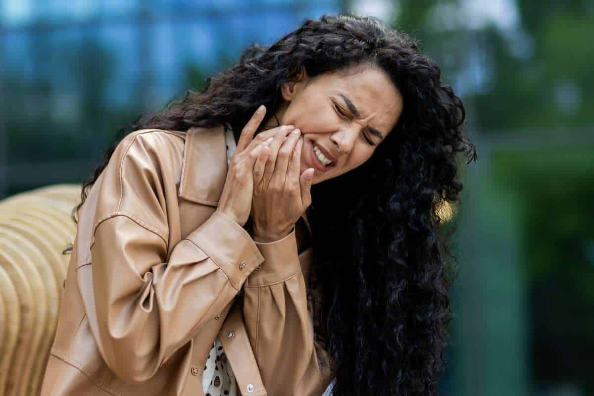 Woman holding her cheek in discomfort, illustrating tooth sensitivity after dental cleaning.