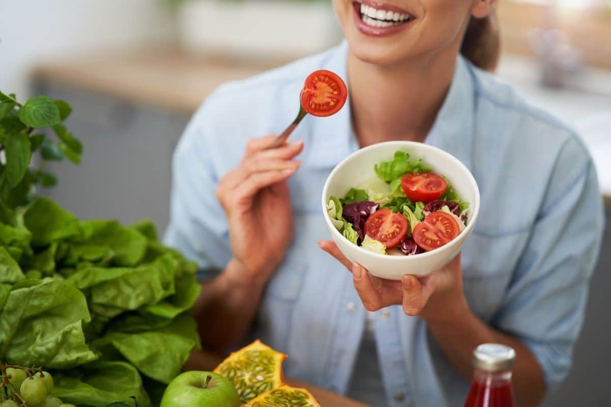 Woman holding a fresh salad bowl with tomatoes and greens, promoting healthy eating after dental surgery.
