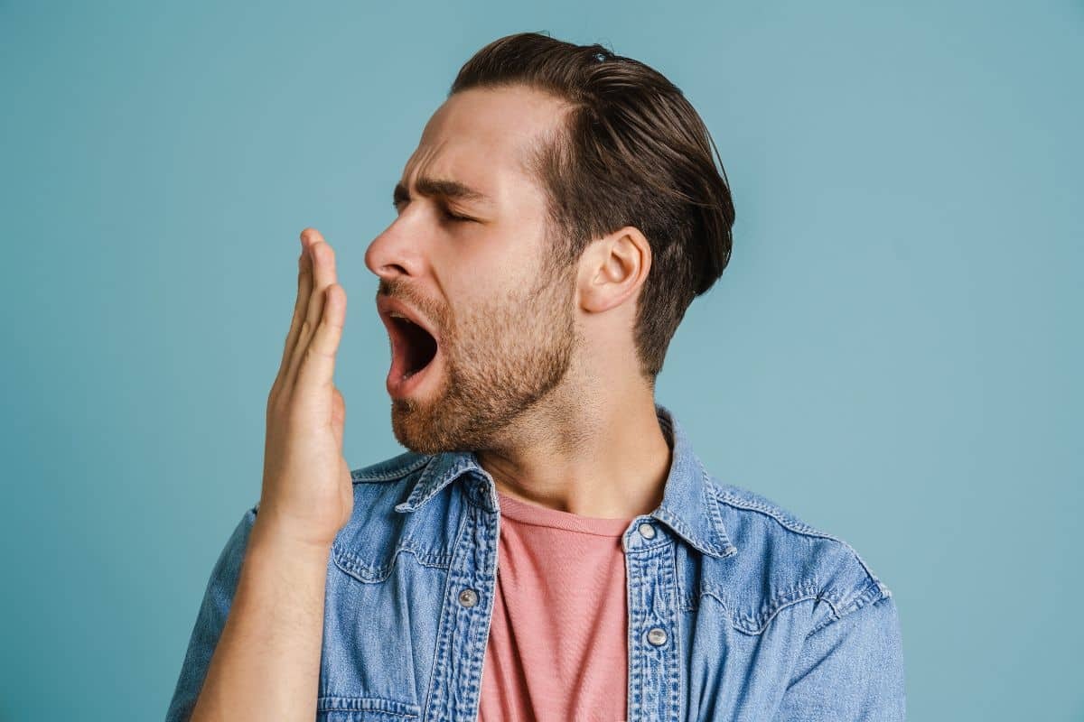 Man checking breath odor by holding hand to mouth against blue background.