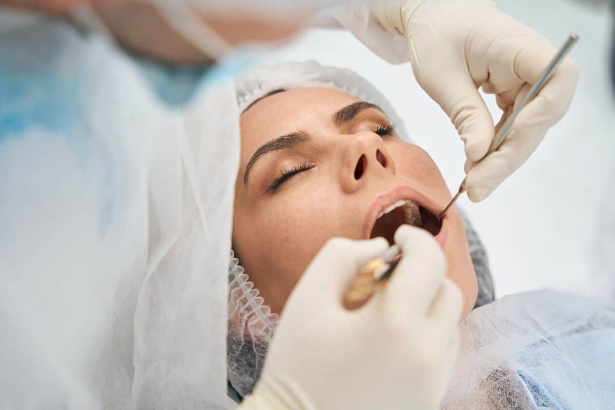 Dentist examining patient's teeth during dental procedure with gloved hands and instruments.